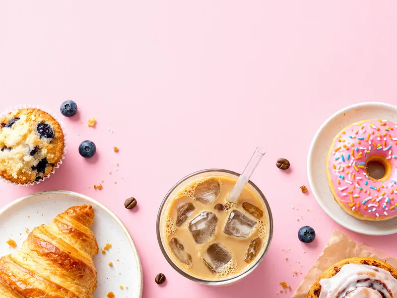 Overhead flat lay of iced coffee and pastries on pastel pink