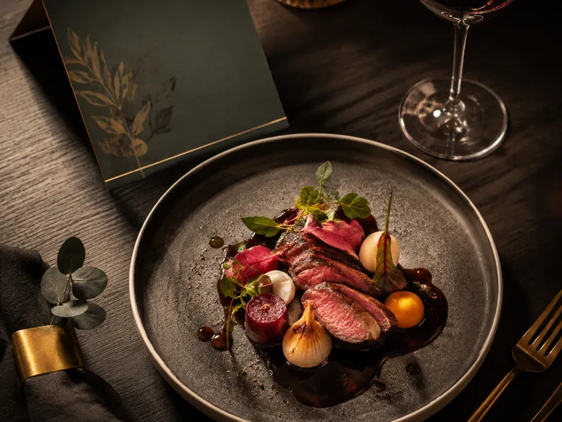 Plated dish on a dark table beside a folded menu card and a glass of wine